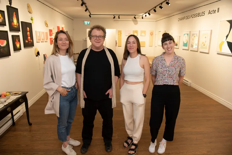 L’artiste et trois personnes devant un mur d’œuvres, en salle d’exposition