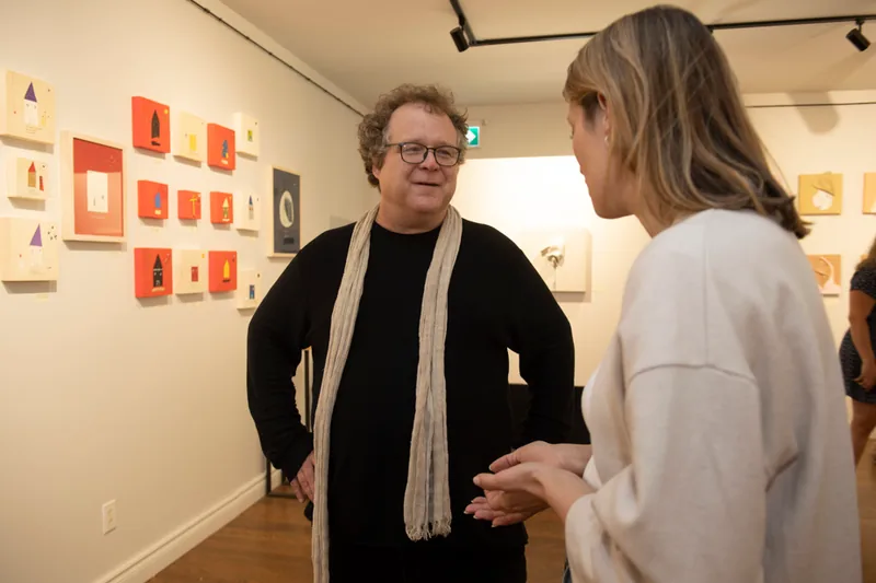 L’artiste en conversation avec une visiteuse devant un mur de petits formats rouges