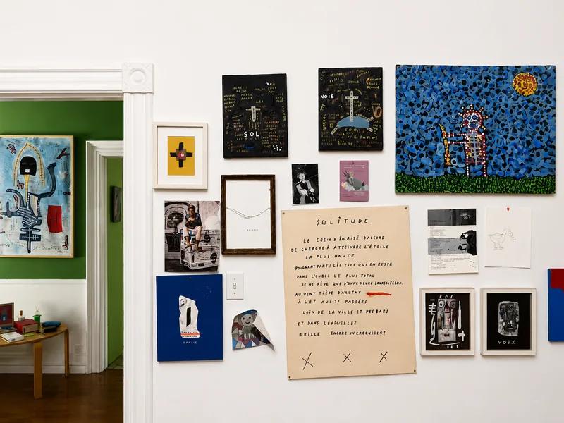 Mur d’atelier couvert d’œuvres encadrées, de dessins et d’un poème dactylographié