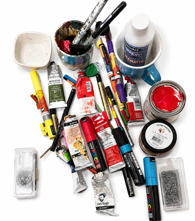 Tubes de peinture, marqueurs, pinceaux et pots disposés à plat sur fond blanc